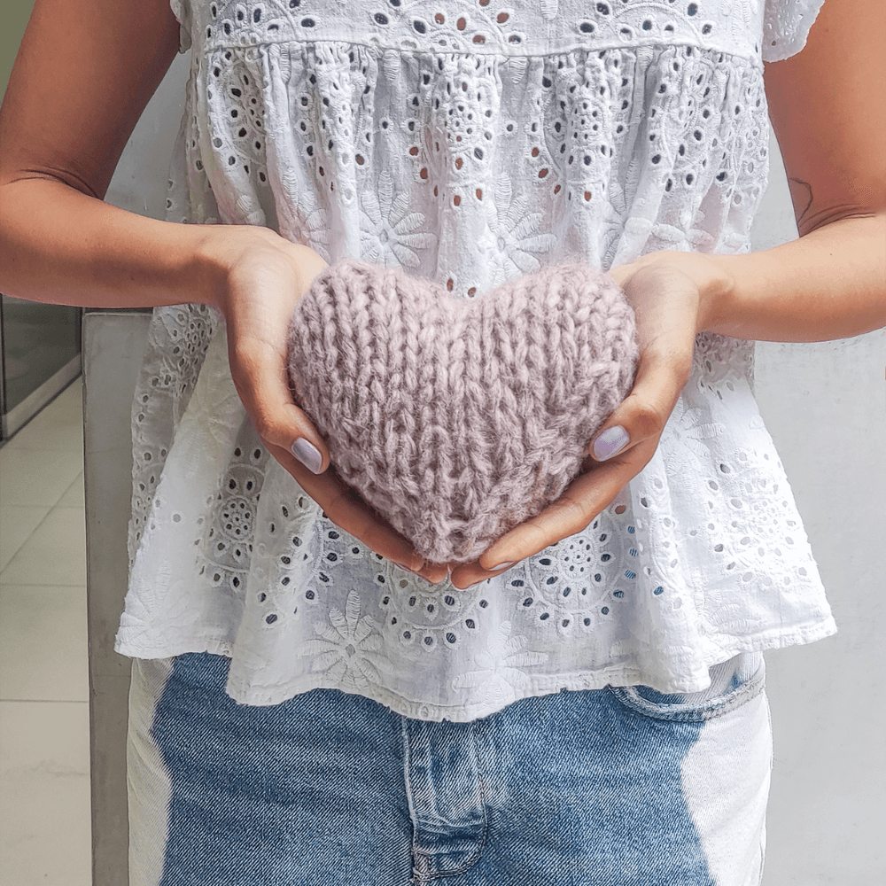 Person holding a knitted heart-shaped object against a neutral background