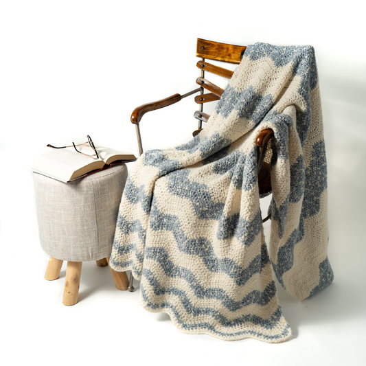 Textured blanket draped over a wooden chair with an open book and glasses on a small table.