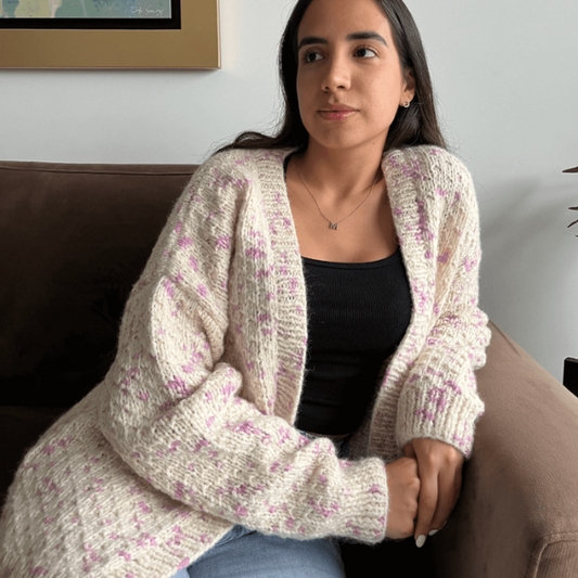 woman wearing a white cardigan with lavender details sitting on a couch