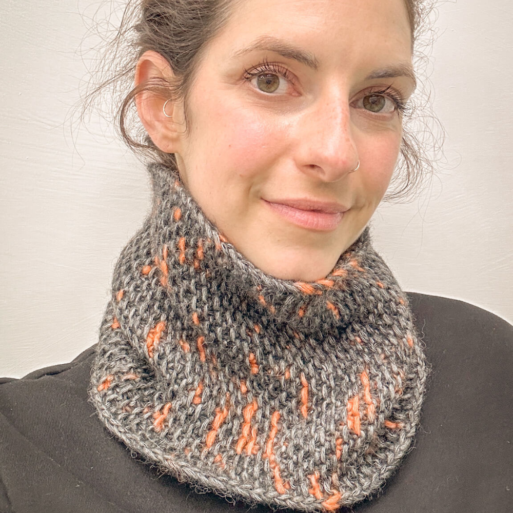 Woman wearing a gray and orange patterned cowl against a plain background