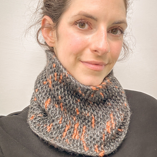 Woman wearing a gray and orange patterned cowl against a plain background