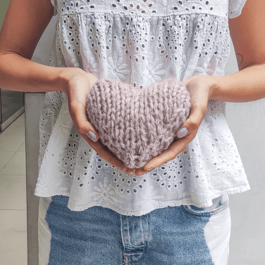 Person holding a knitted heart-shaped object against a neutral background