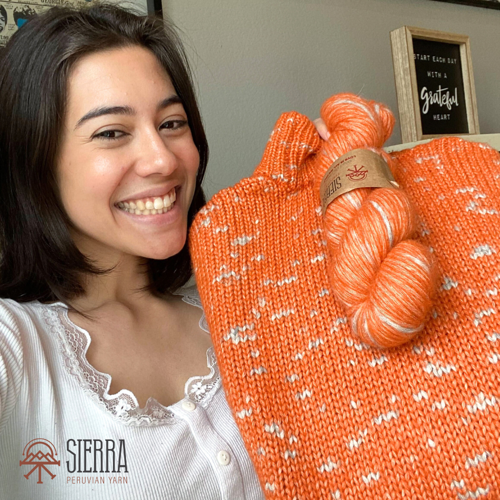 Woman smiling and showing a finished knitting kit from Sierra Yarn with one additional andean spirit skein both on color orange grey