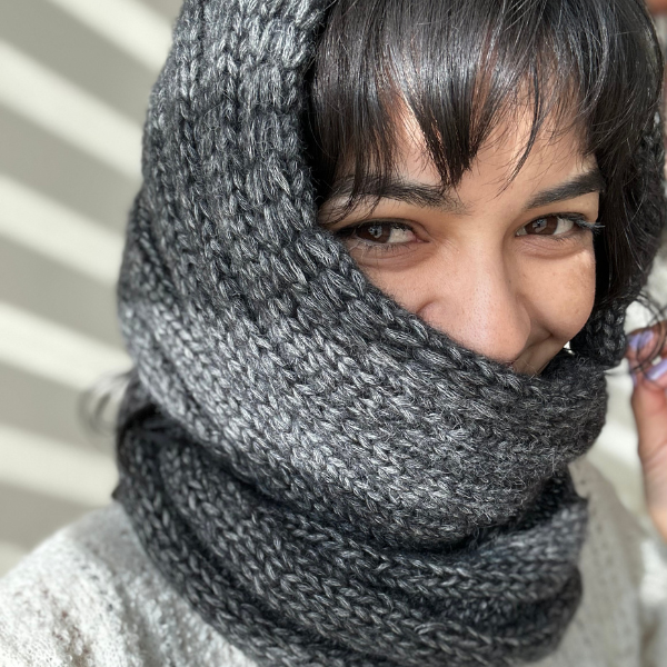Woman wearing a gray knitted scarf covering her face, with a blurred background.