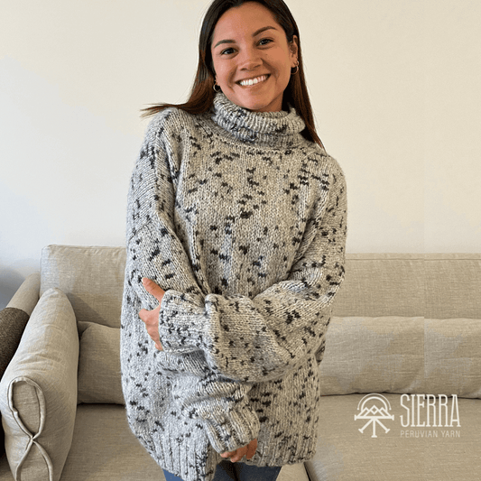 Woman wearing a patterned oversized sweater standing in a living room with a sofa in the back