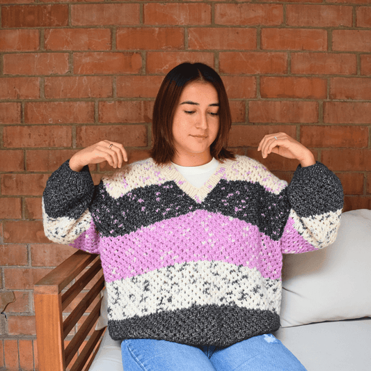 Person wearing a colorful striped sweater sitting against a brick wall.