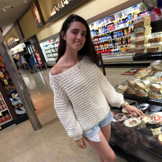 Woman in a white sweater and denim shorts standing in a convenience store.