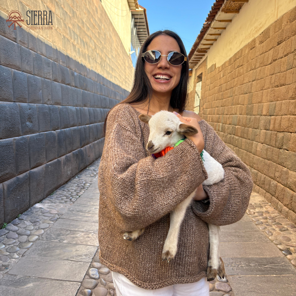Woman holding a lamb in a narrow alleyway with stone walls and a clear sky.